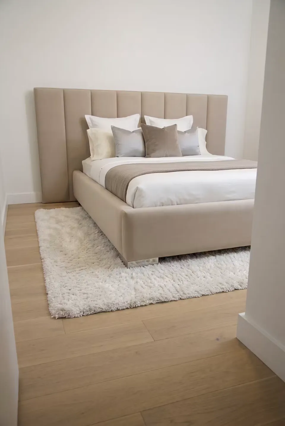 Front angled view of the beige channel bed in a simple white room.