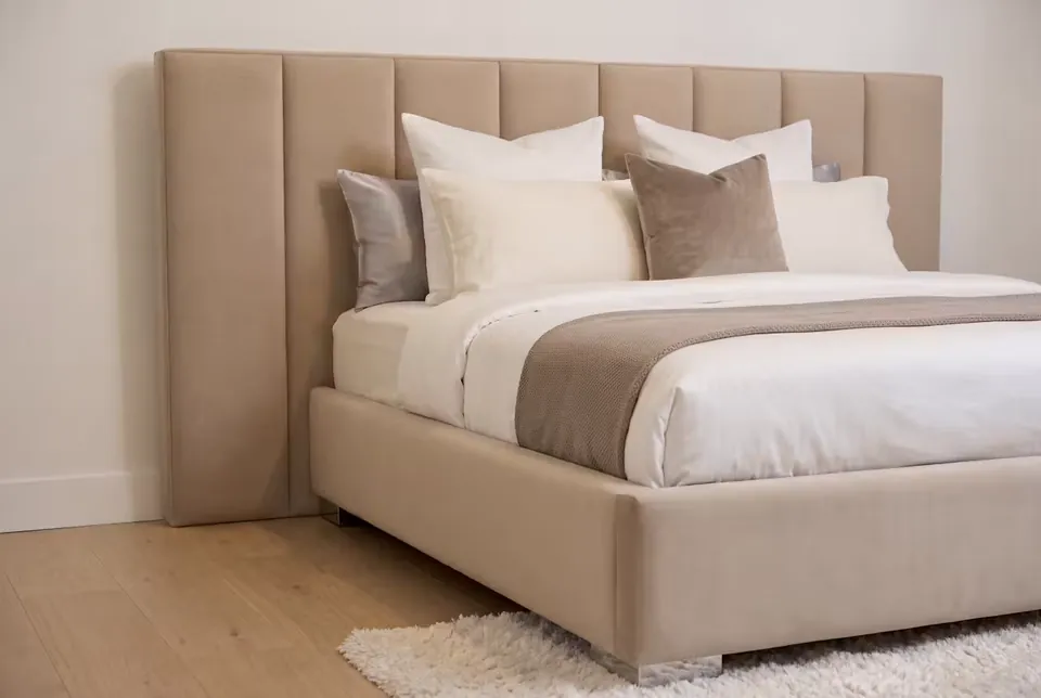 Closer view of the beige bed frame and broad padded headboard channels.