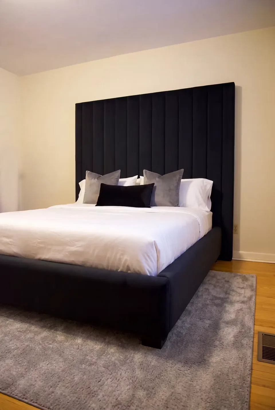 Full view of a black channelled headboard, white bedding and a dark upholstered bed frame