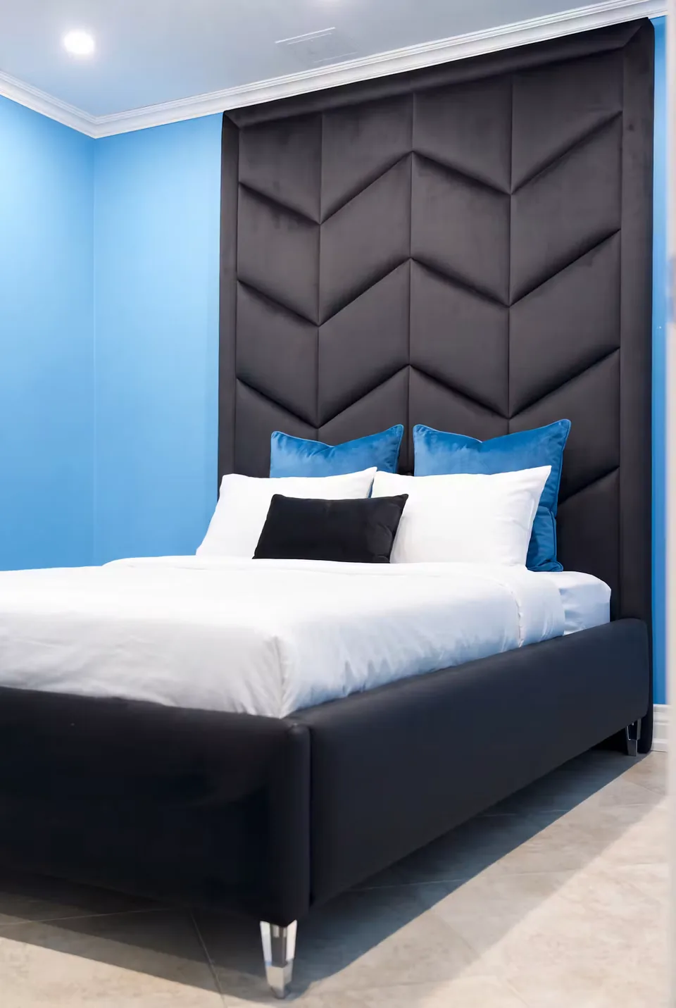 Black upholstered bed beneath a tall chevron headboard against blue walls
