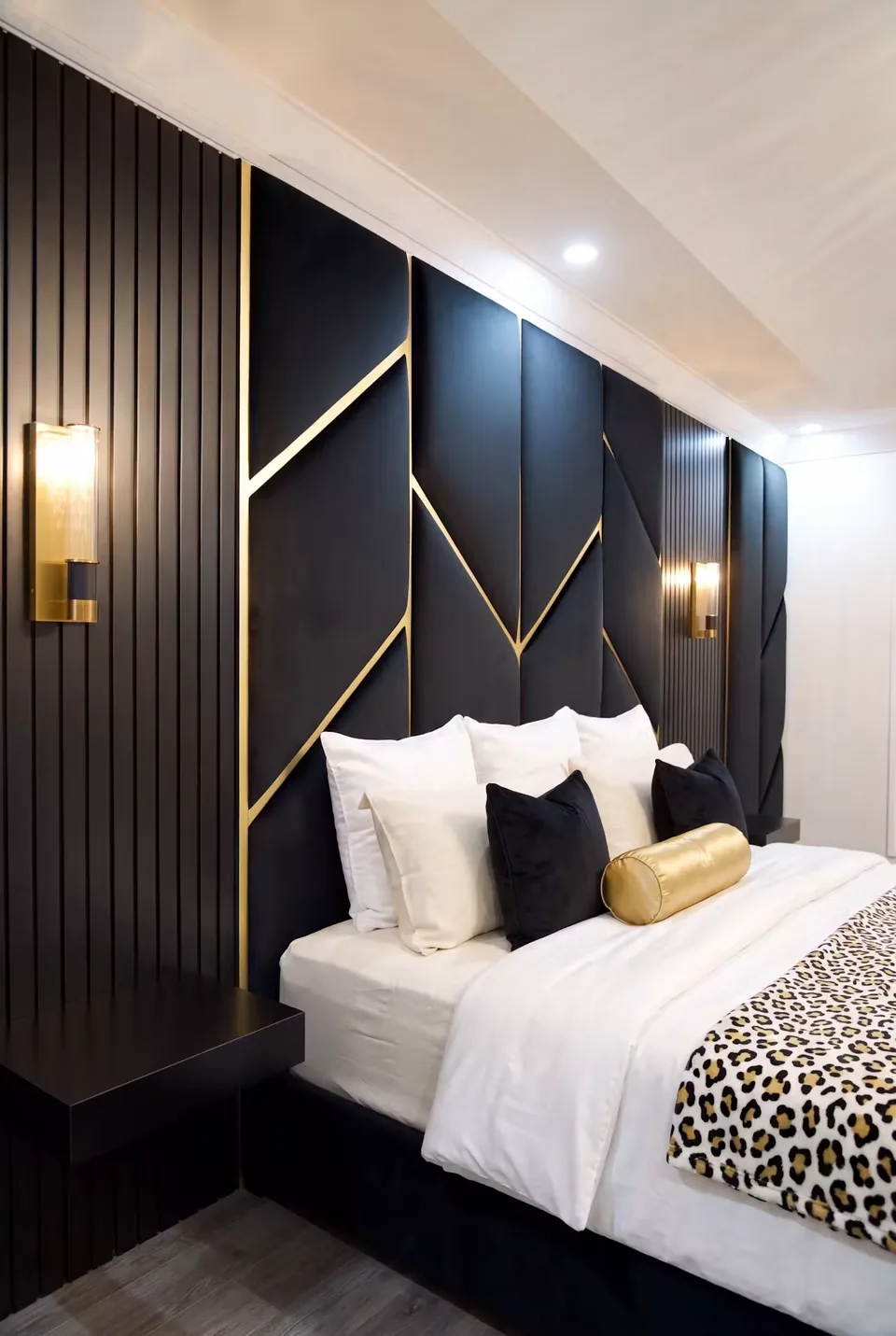 Left angled view of black panels, diagonal gold lines and layered pillows above the bed.