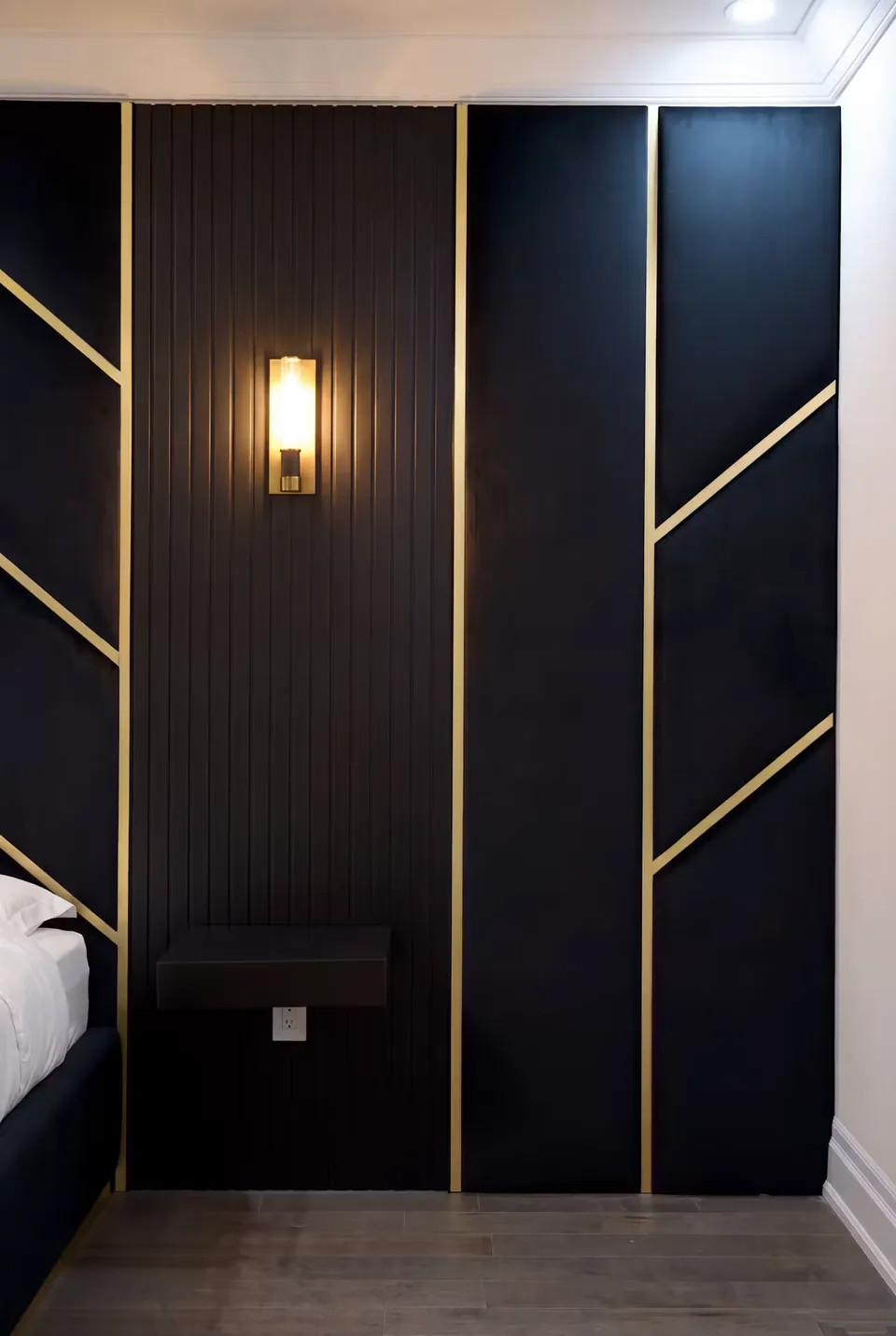 Detail of a warm wall light on dark fluted upholstery beside gold-divided black panels.
