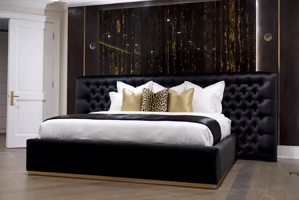 Full front view of a black button-tufted bed beneath a dark gold-veined wall.