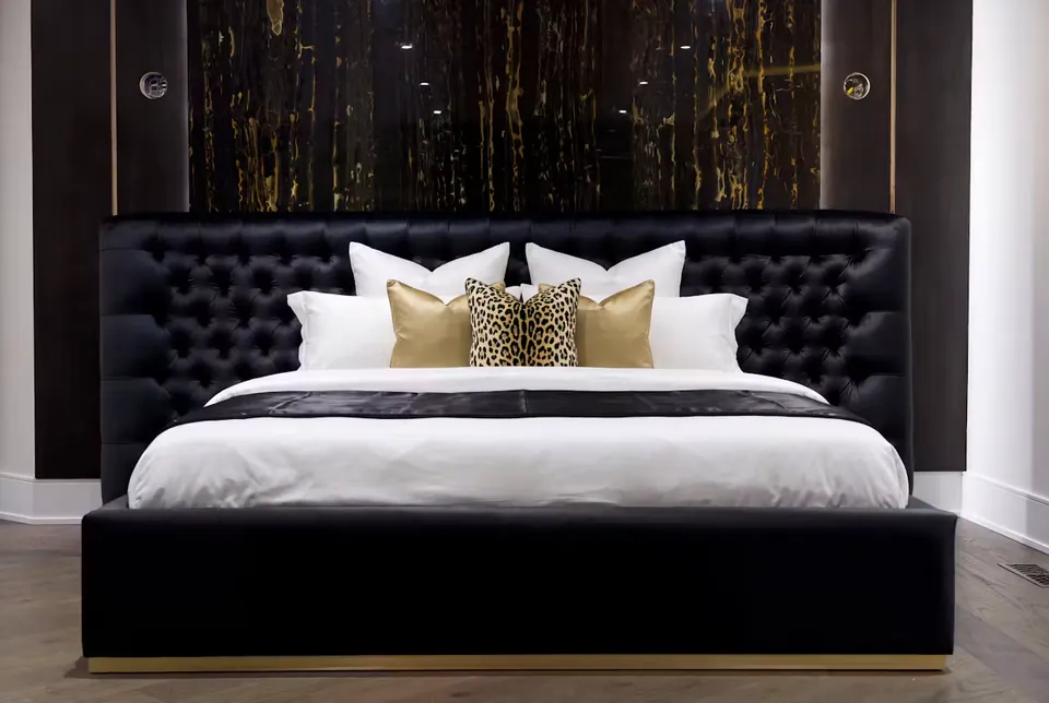 Front view of the black tufted bed with white bedding beneath a gold-veined wall.