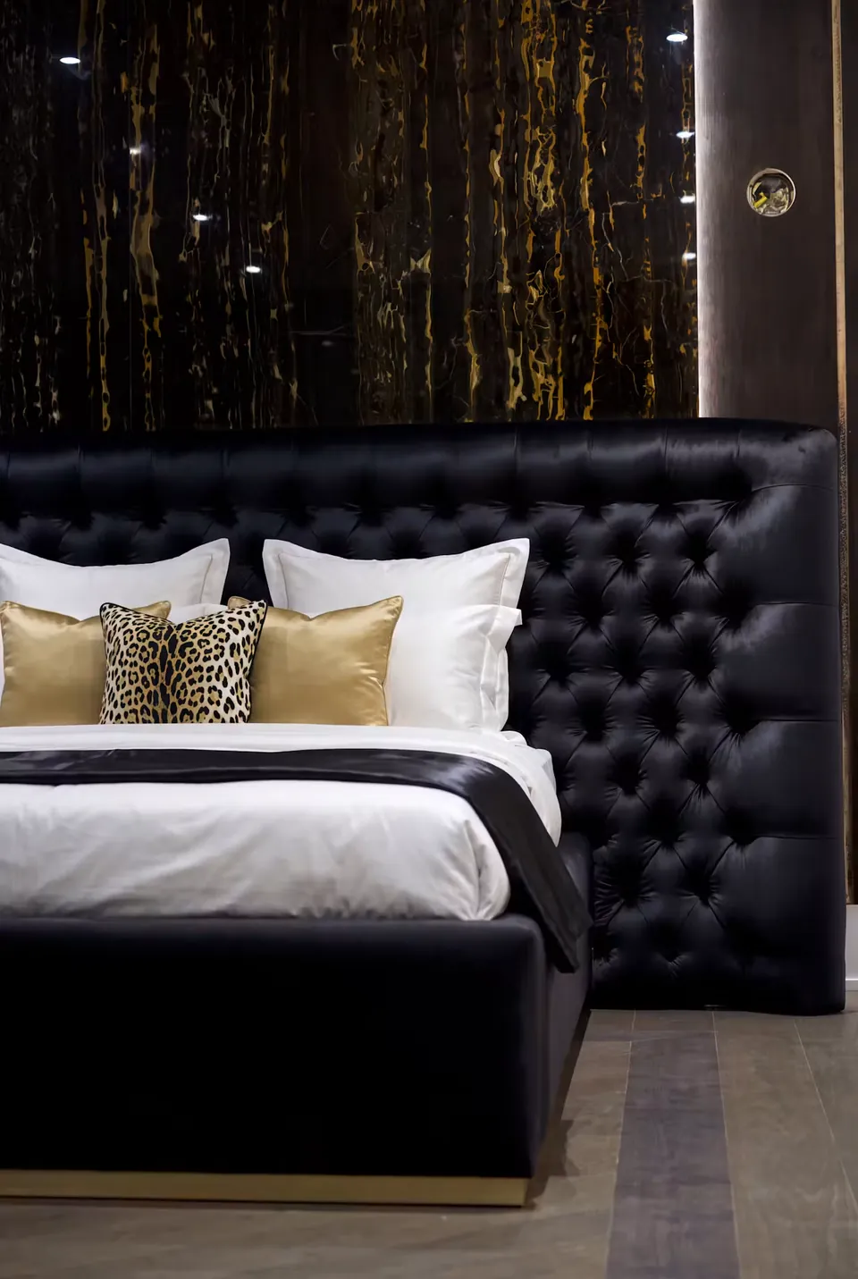 Front detail of the wide black button-tufted headboard and pale cushions.