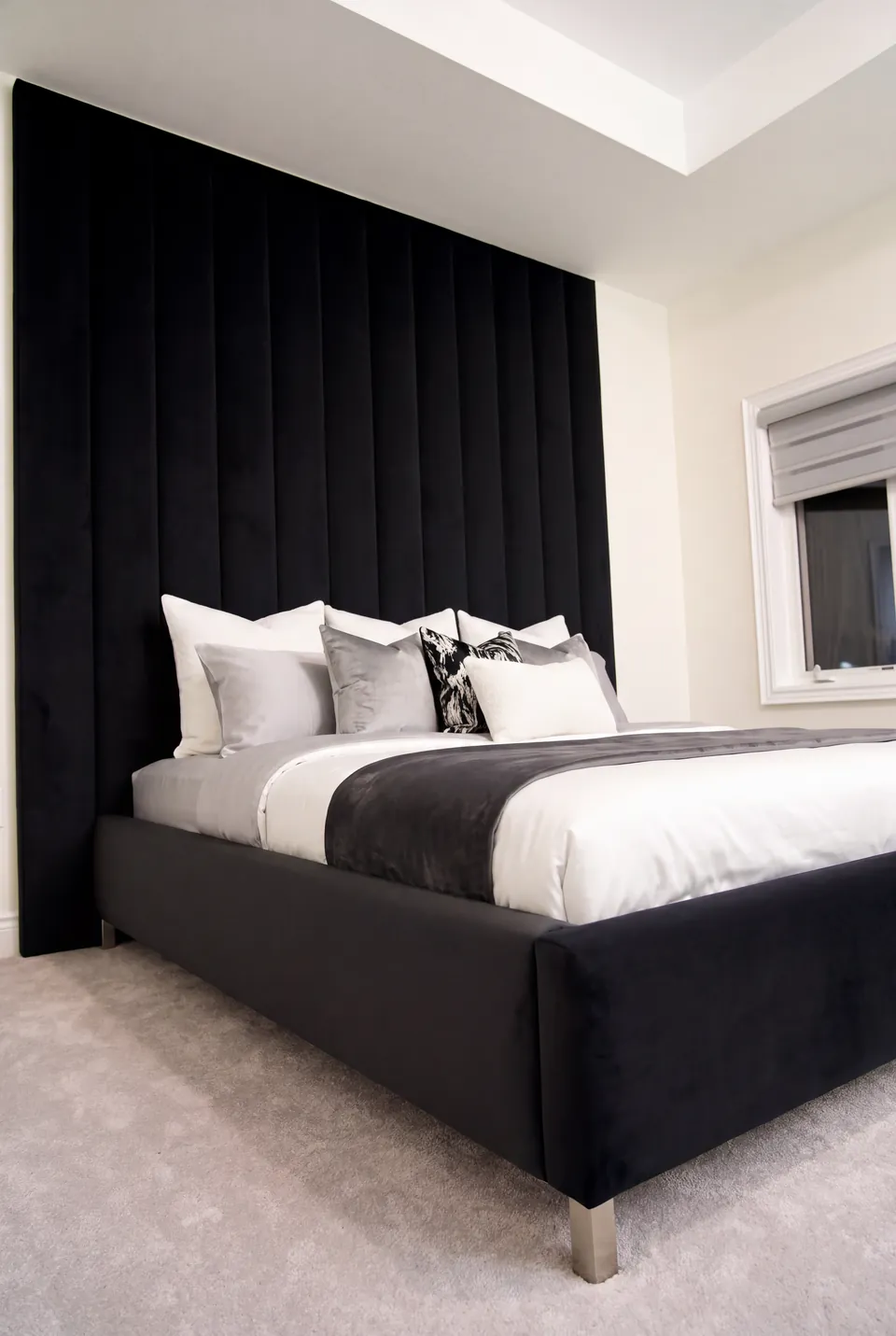 Angled view of a black upholstered bed with white bedding and slim metallic legs.