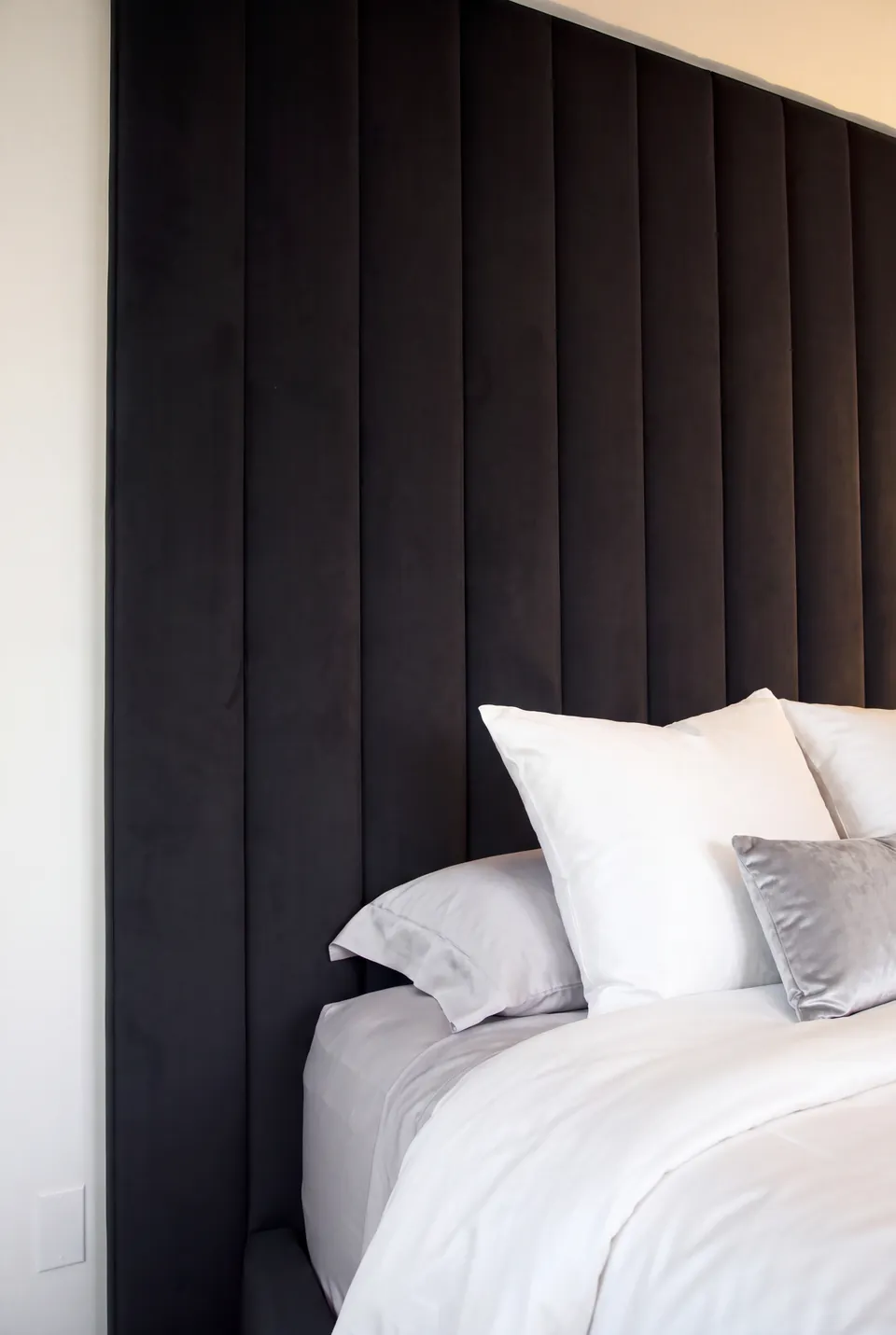 Close view of white pillows against the black channelled headboard wall.