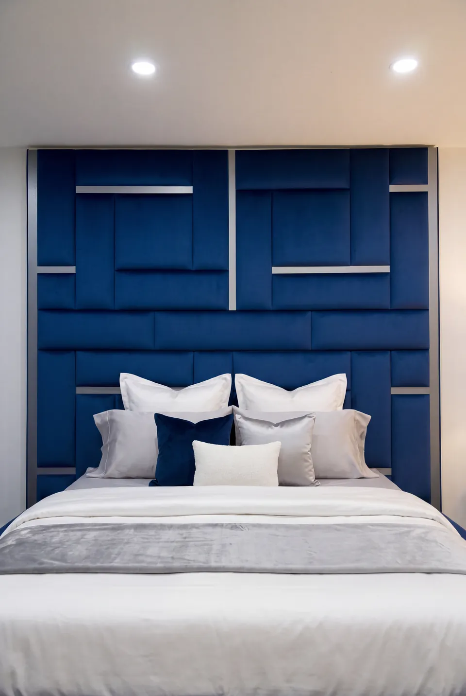 Front view of a blue bed wall with white bedding and gold linear accents.