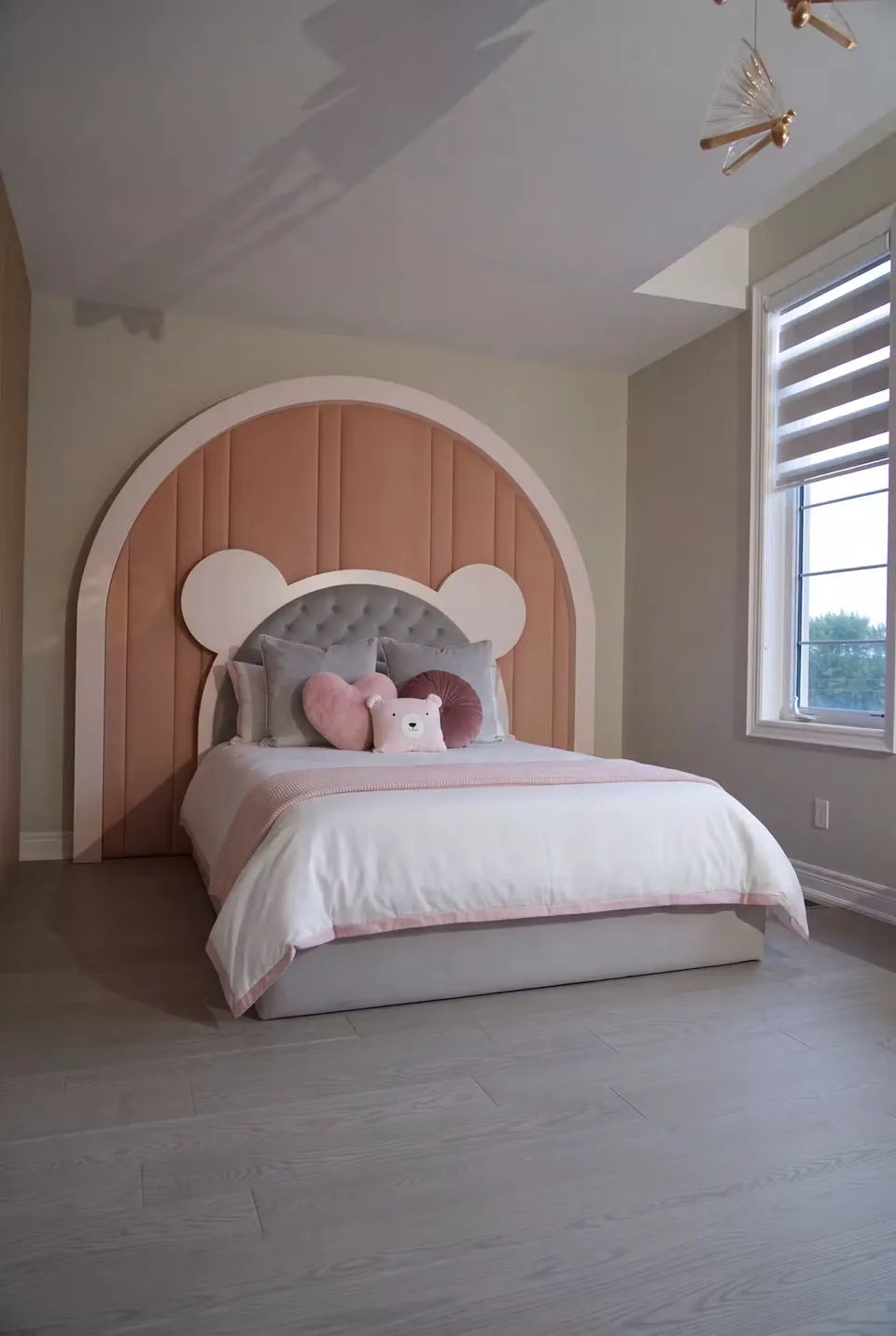 Wide angled view of the pale bed beneath the blush arch and grey bear headboard