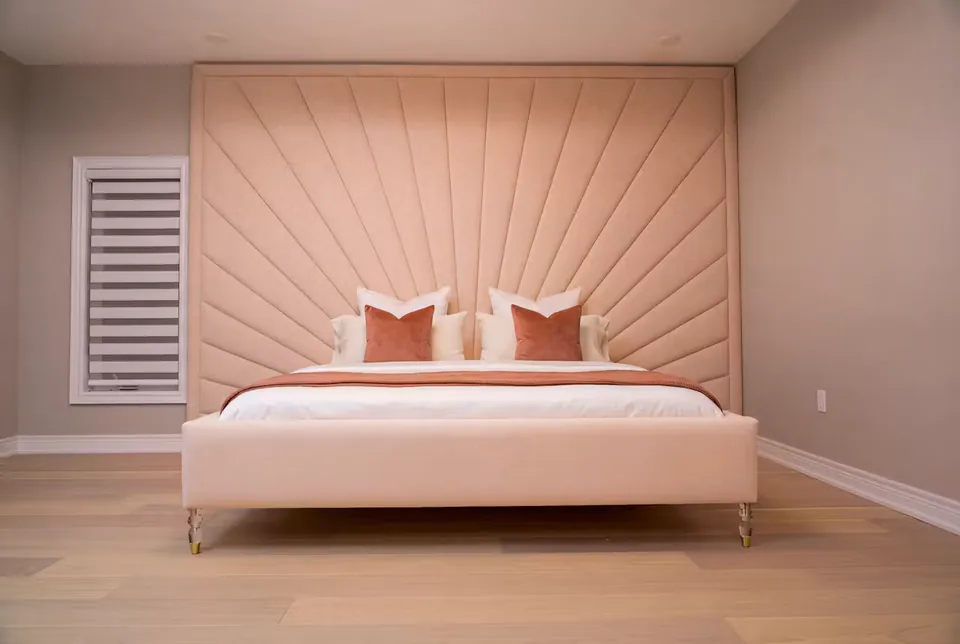 Blush upholstered bed below a wall-sized headboard with rays spreading from its lower corner