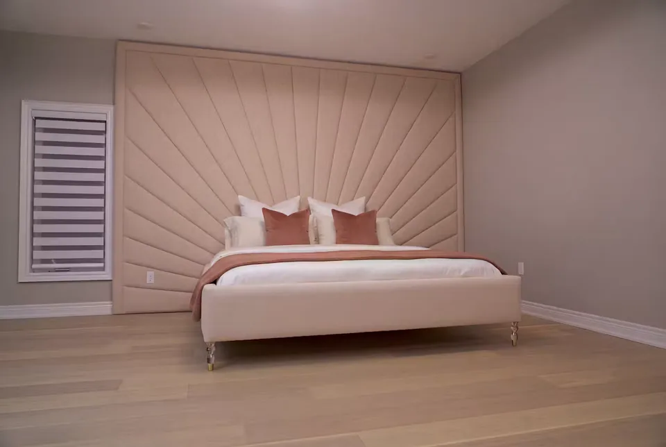 Full view of a pale pink bed with a radiating padded headboard and wood floor