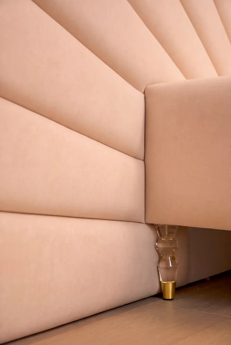 Detail of a decorative clear-and-gold-toned leg below the blush bed frame