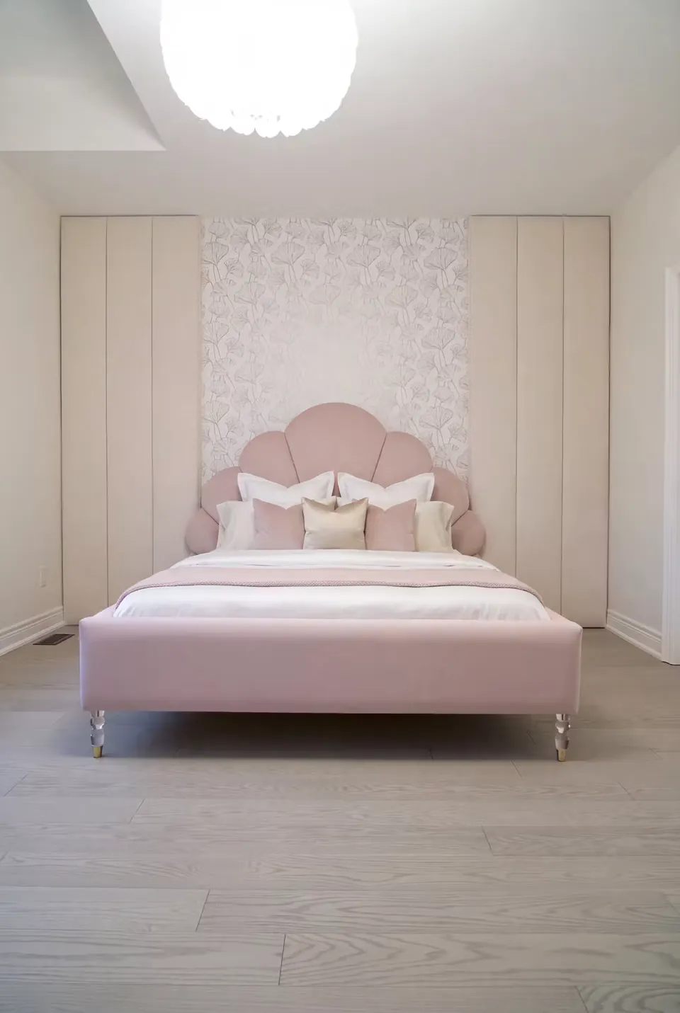 Full view of a blush upholstered bed with a petal-shaped headboard between pale wardrobes.