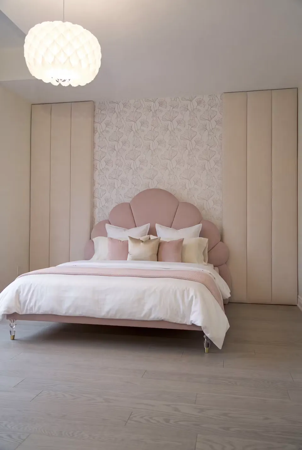 Wide front view of the blush petal bed between tall wardrobes and floral wallpaper.