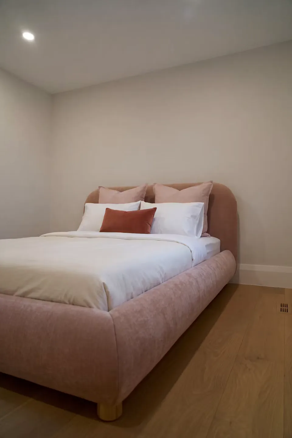 Full angled view of the blush bed and curved padded footboard
