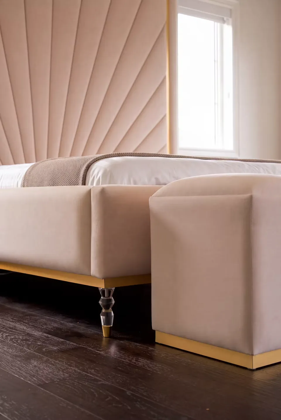 Detail of the blush padded bench, gold edging and clear bed feet beside the sunray headboard.