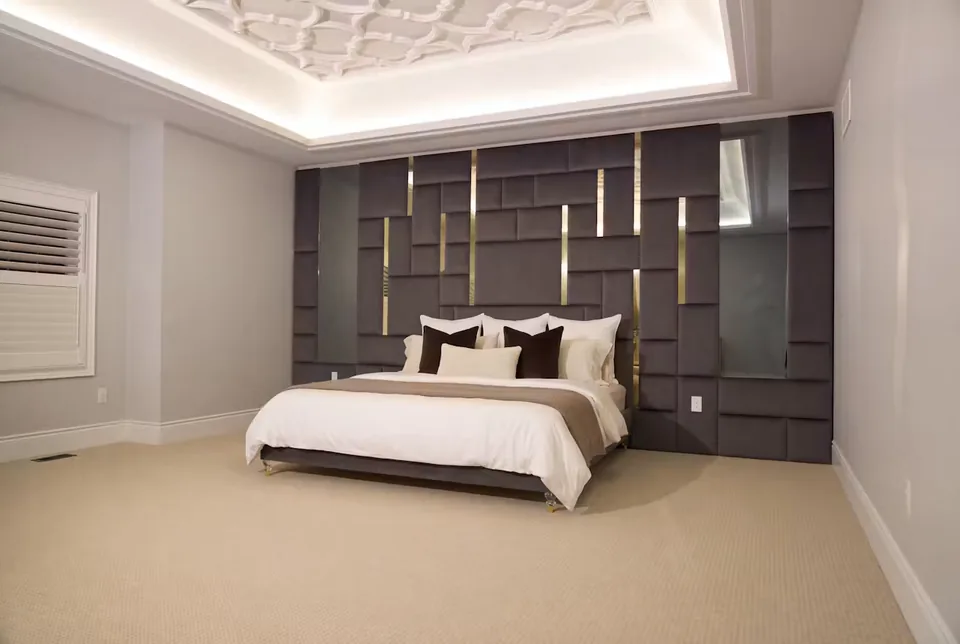 Full angled room view of the dark upholstered bed, geometric wall and patterned ceiling.