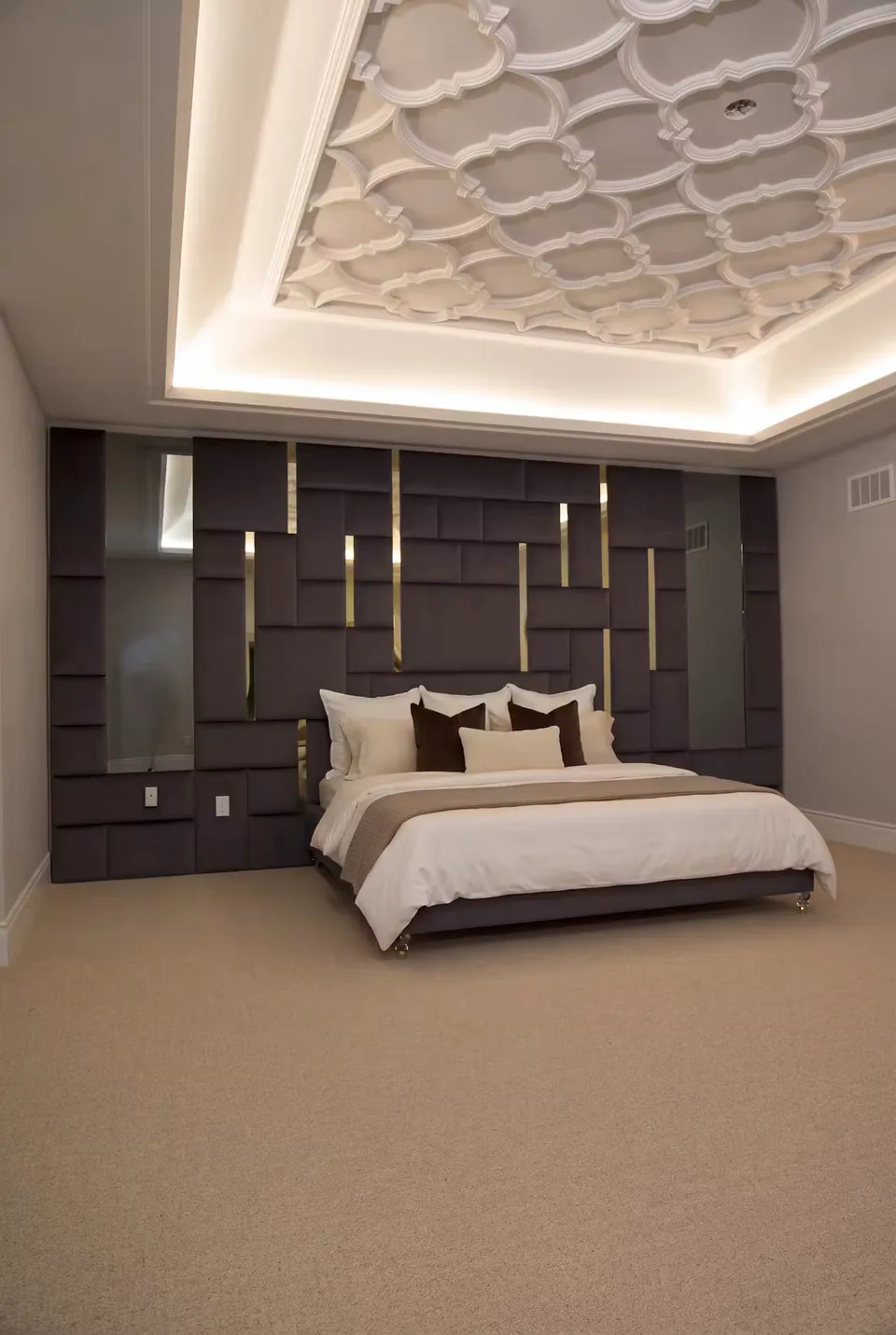 Wider vertical view of the charcoal bed and gold-accented padded wall beneath a detailed ceiling.