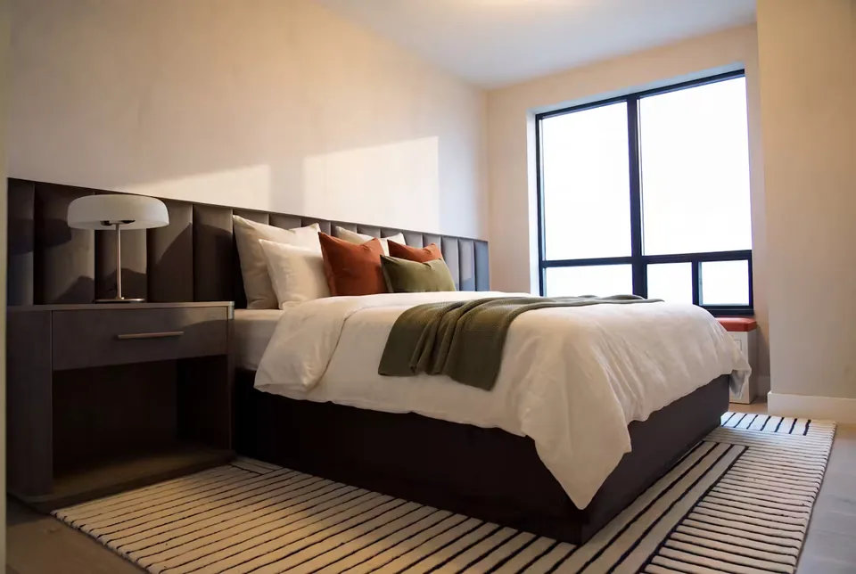 Charcoal upholstered bed with broad vertical channels beside a tall window