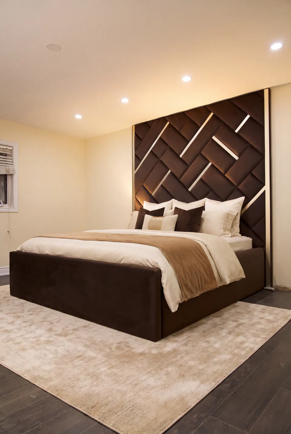 Full view of a brown upholstered bed beneath a woven geometric wall with gold accents.