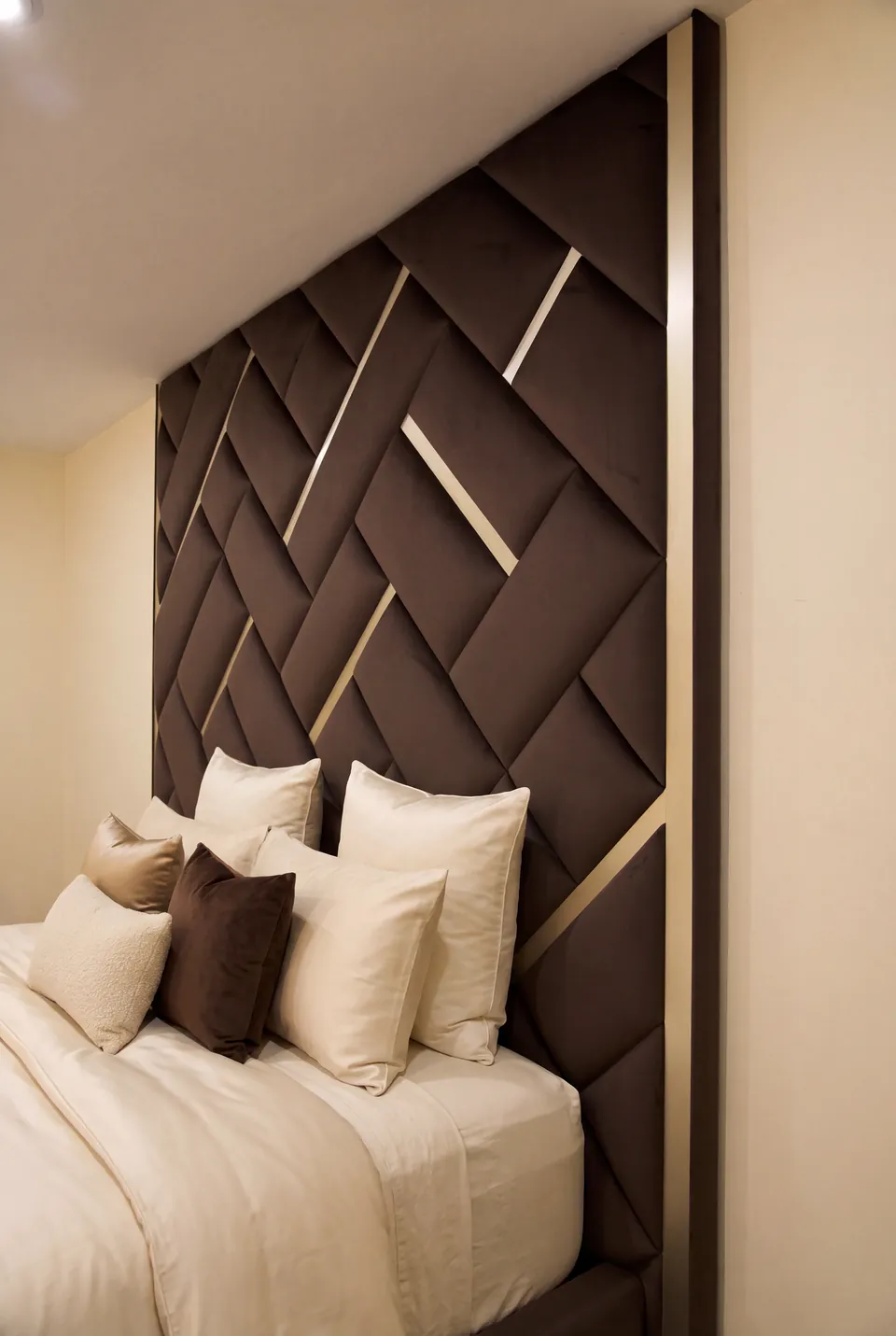 Angled view of the brown geometric headboard and layered neutral pillows.