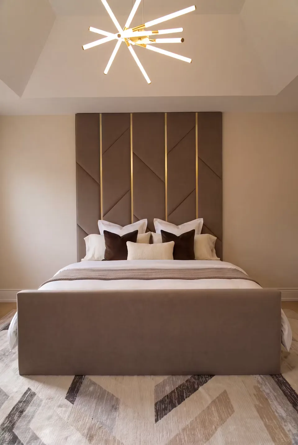 Full front view of a cocoa upholstered bed and tall angular wall panels divided by gold strips.