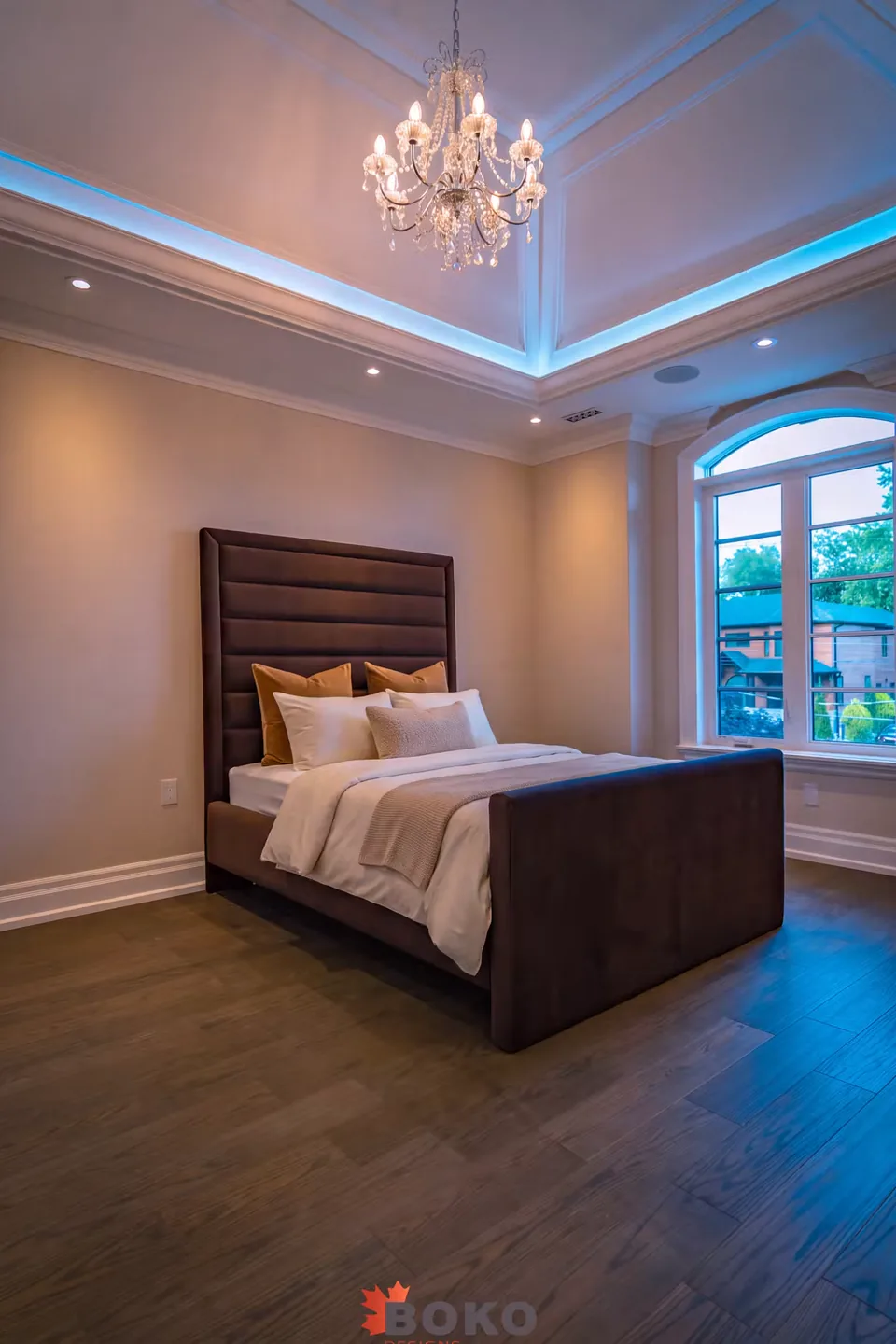 Full room view of the cocoa bed and tall footboard beside an arched window
