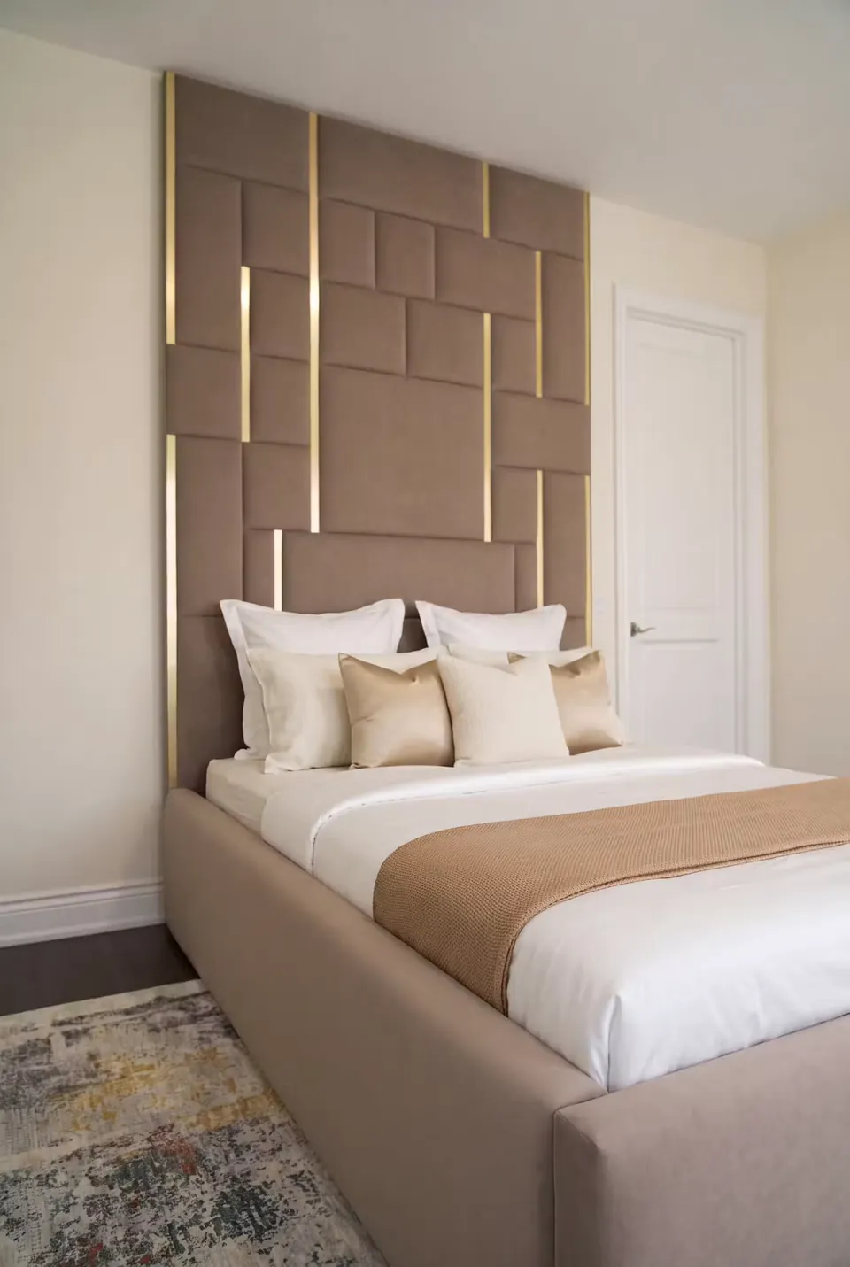 Angled view of a cocoa upholstered bed beneath staggered brown wall panels with gold accents.