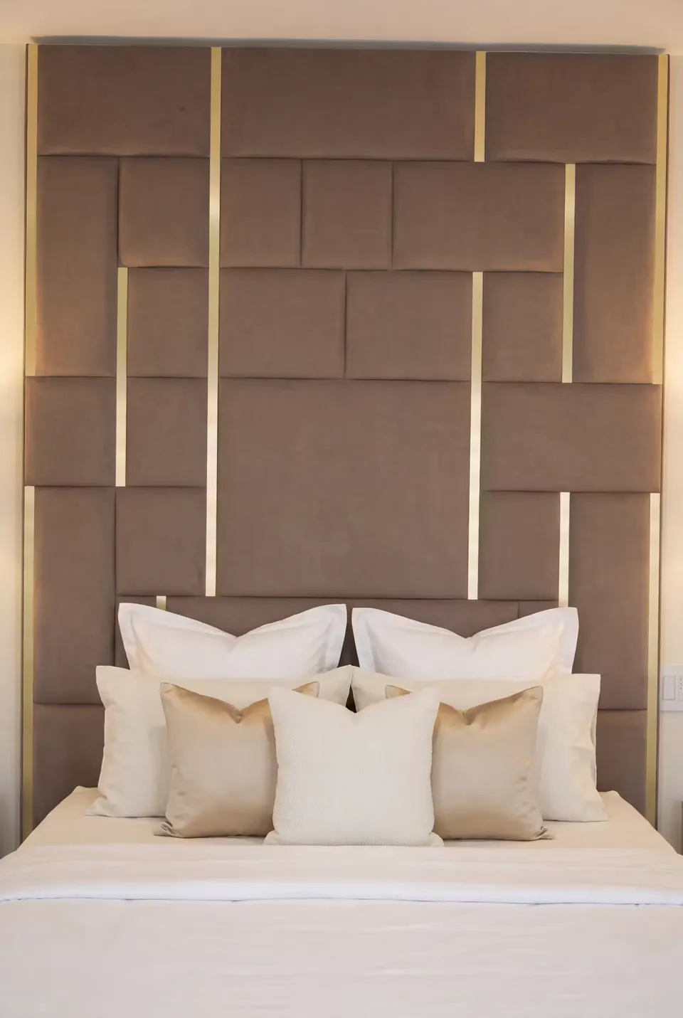 Front view of tall cocoa padded rectangles and gold strips above white and cream pillows.