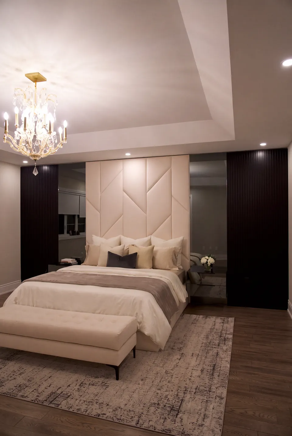 Wide view of a cream bed and matching bench beneath angular upholstered wall panels.