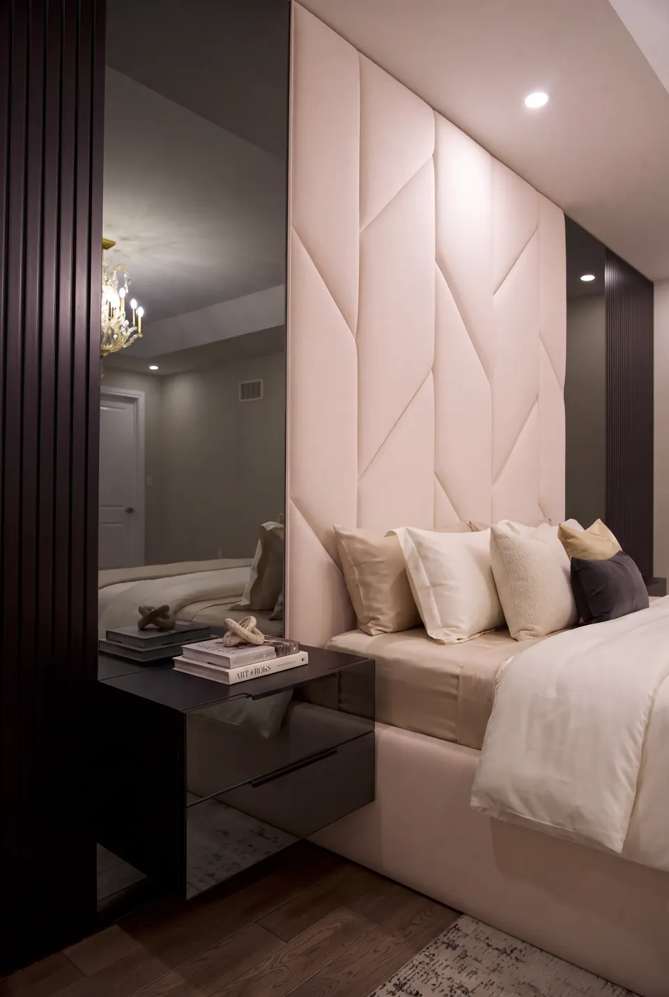 Angled view of a cream upholstered headboard beside a mirror and floating bedside drawer.