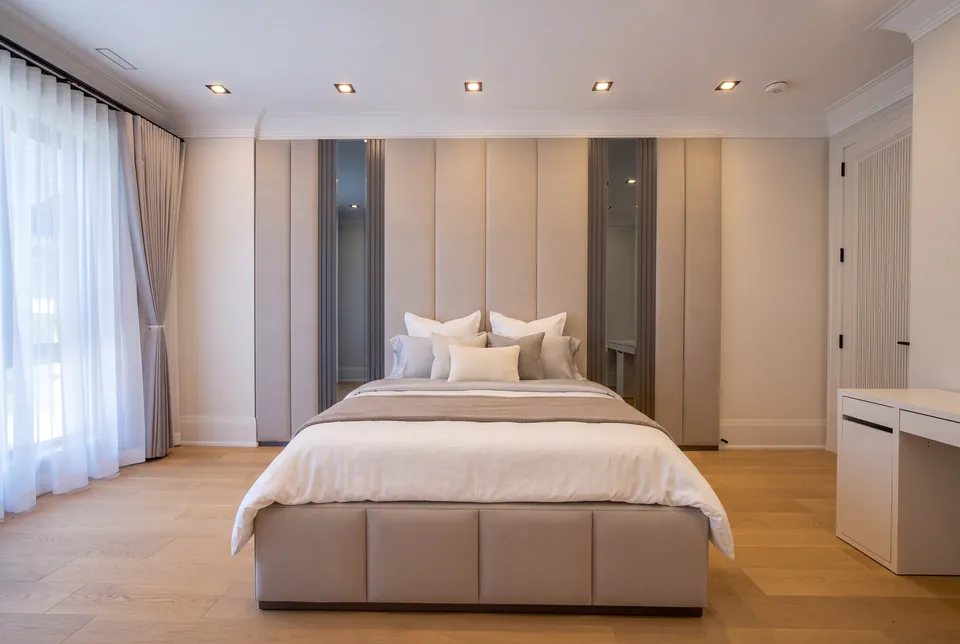 Full front view of a cream upholstered bed with a divided base and tall mirrored panel wall.