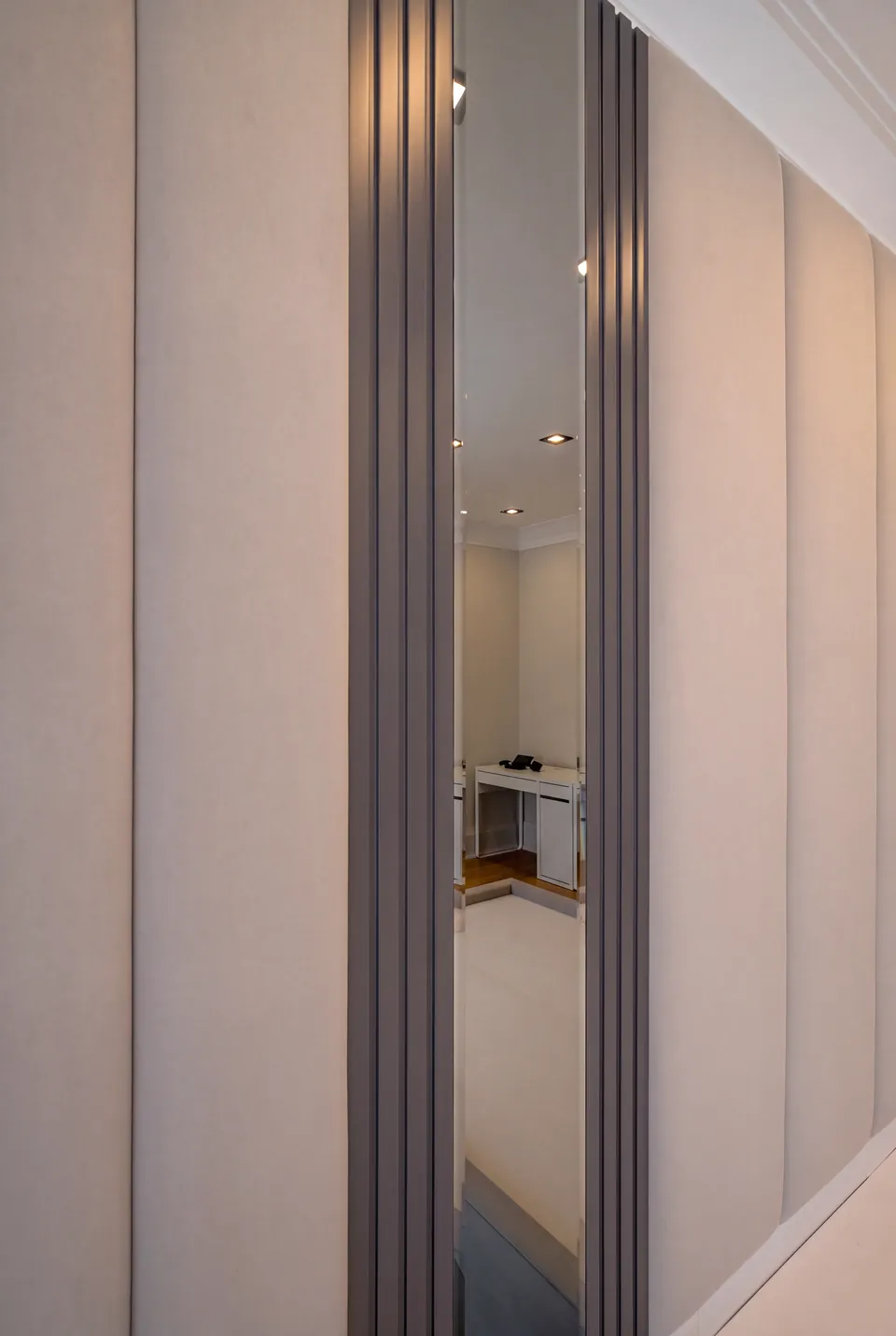 Detail of a cream upholstered panel beside dark mirror glass and narrow fluting.