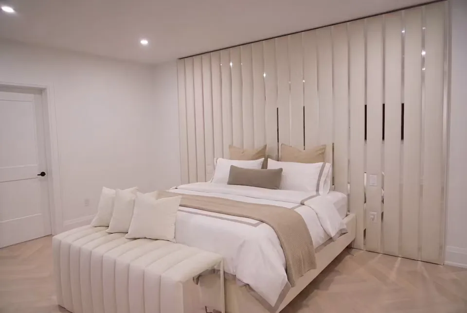 Full bedroom view with a cream bed, upholstered bench and mirrored panel wall