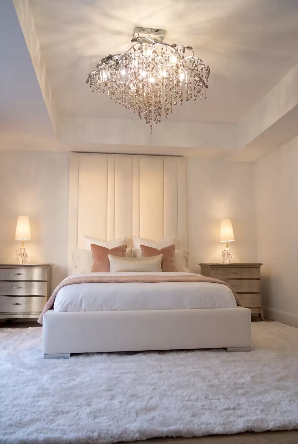 Front view of a pale panelled bed and rounded footboard beneath a glass chandelier