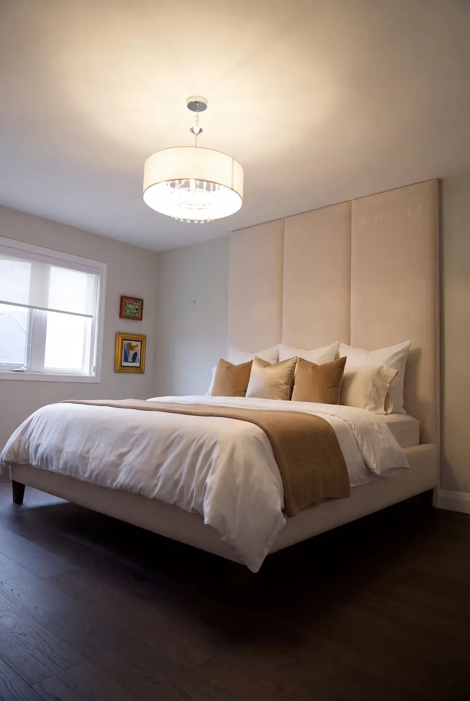 Full angled view of a cream upholstered bed beneath three tall wall panels with caramel bedding.