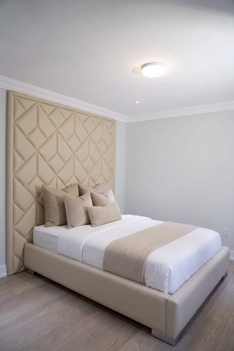 Full view of the cream upholstered bed and woven diamond backdrop
