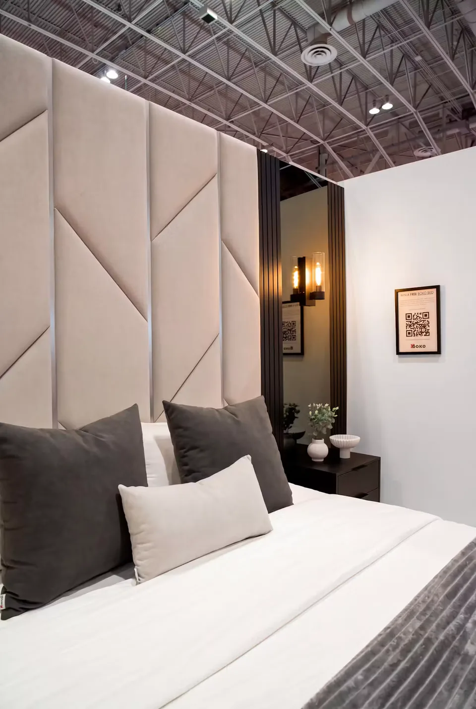 Ivory geometric headboard panels beside a black fluted column, a tall mirror with a wall sconce and a floating black nightstand