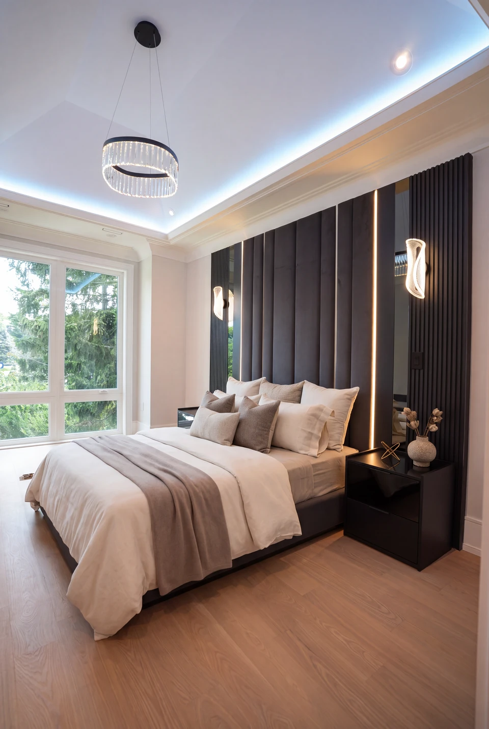 Cream bedding against a tall charcoal upholstered wall with vertical lighting and dark bedside tables.