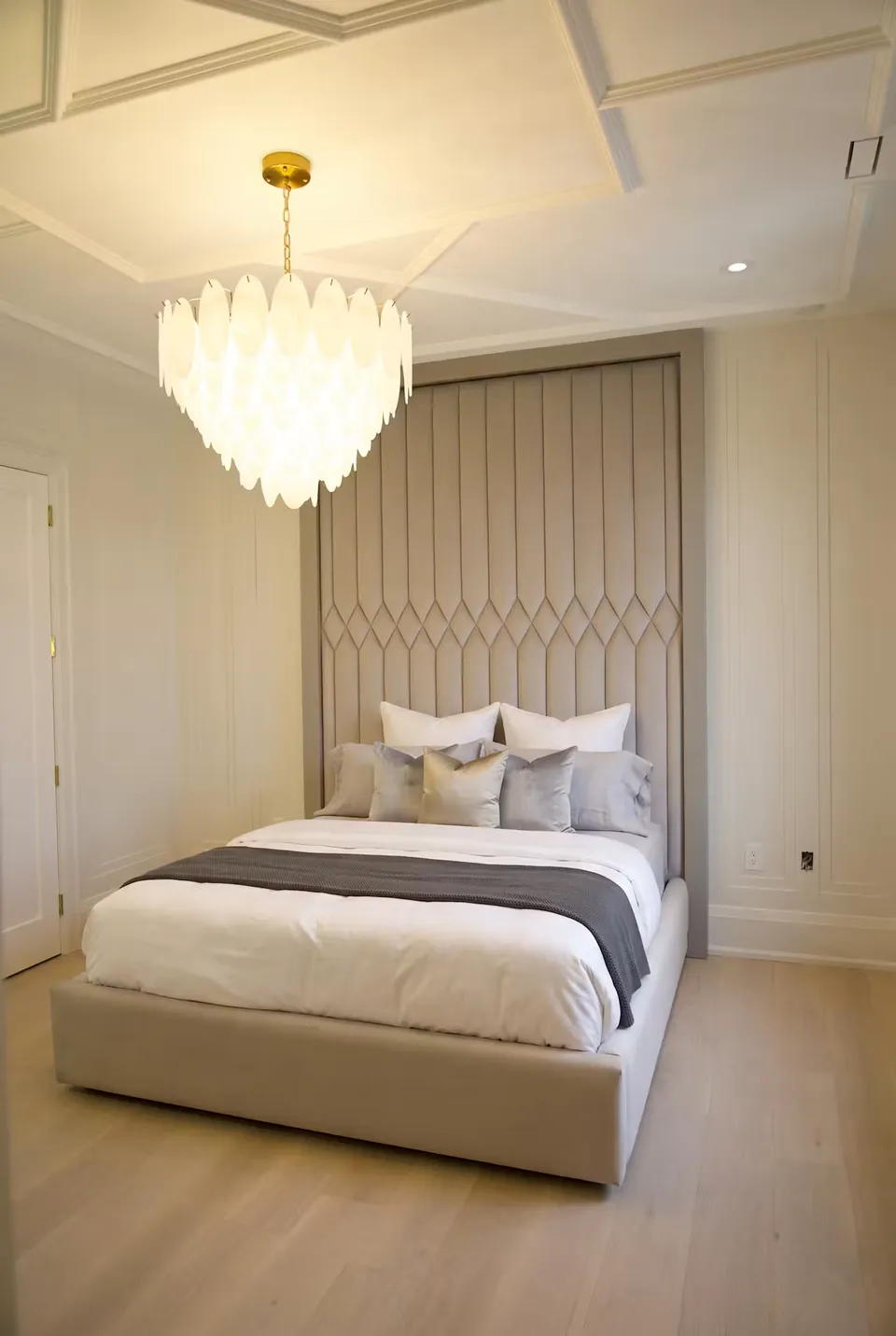 Wide view of the grey bed and diamond-banded headboard under a pale pendant.