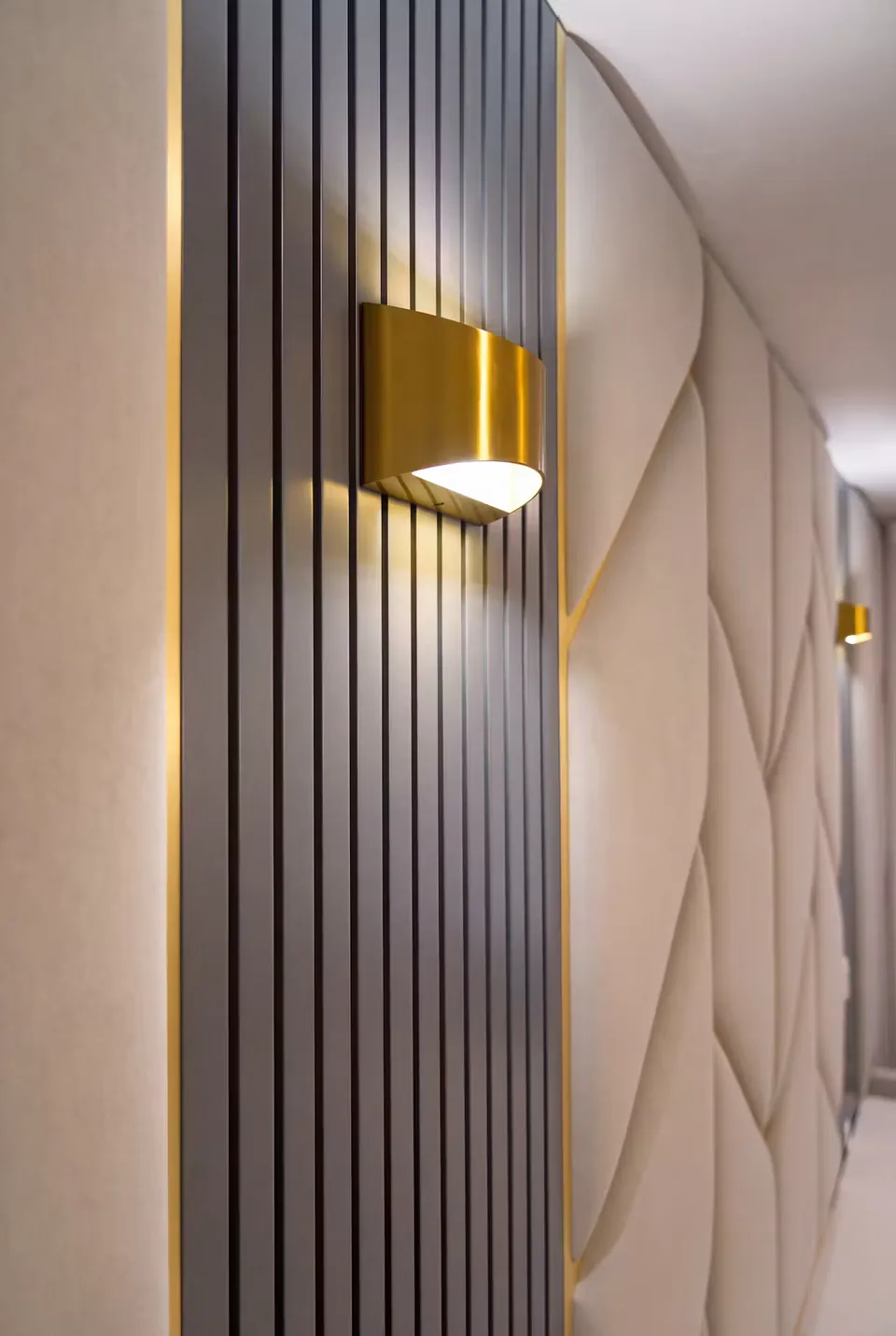 Gold-toned wall light on dark vertical slats beside a padded geometric headboard