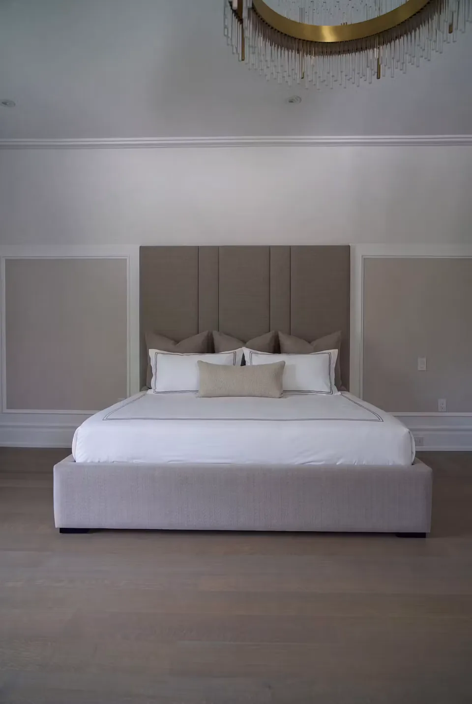 Full front view of the greige upholstered bed against the moulded wall