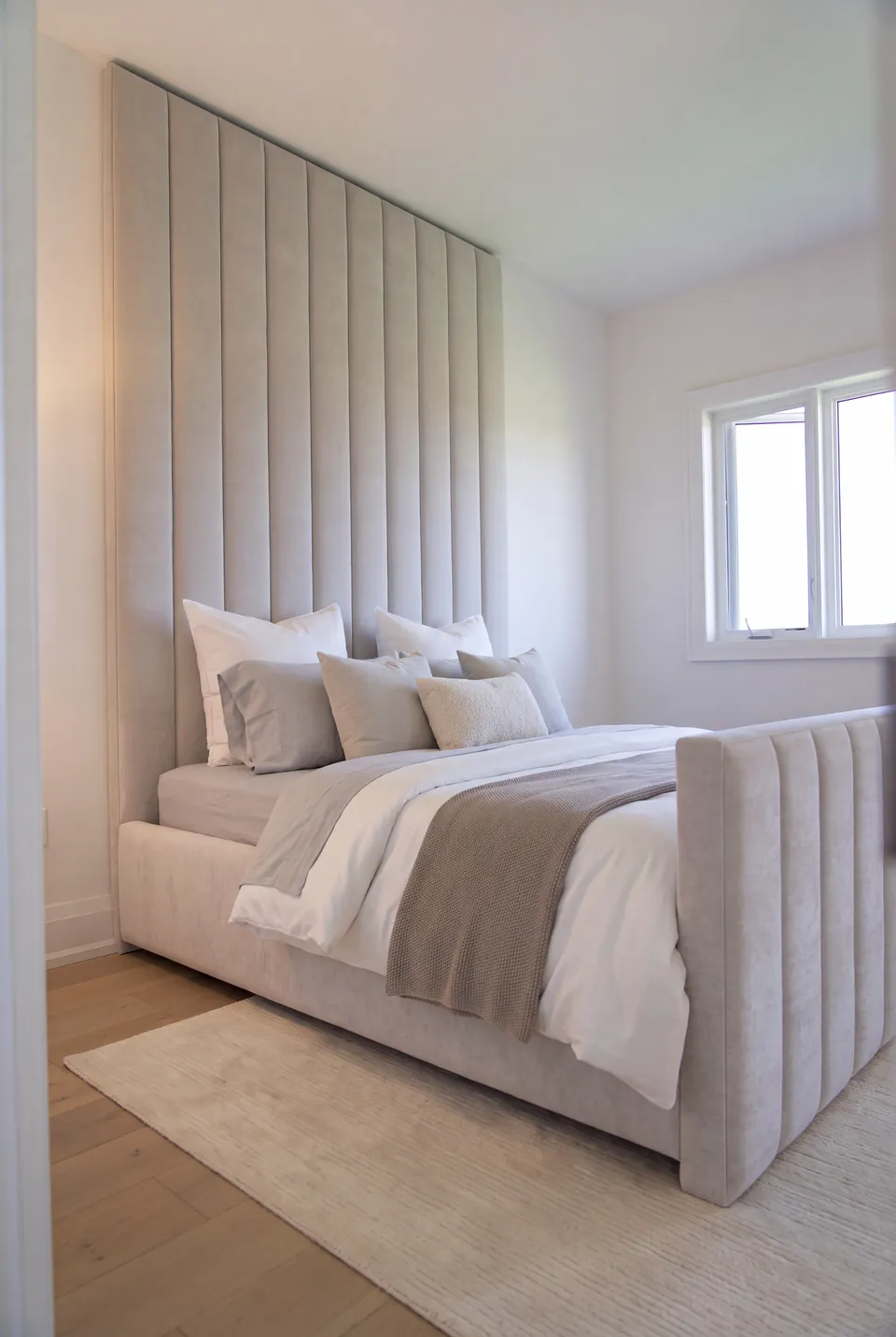 Full angled view of a greige upholstered bed with tall channels and a channelled footboard.