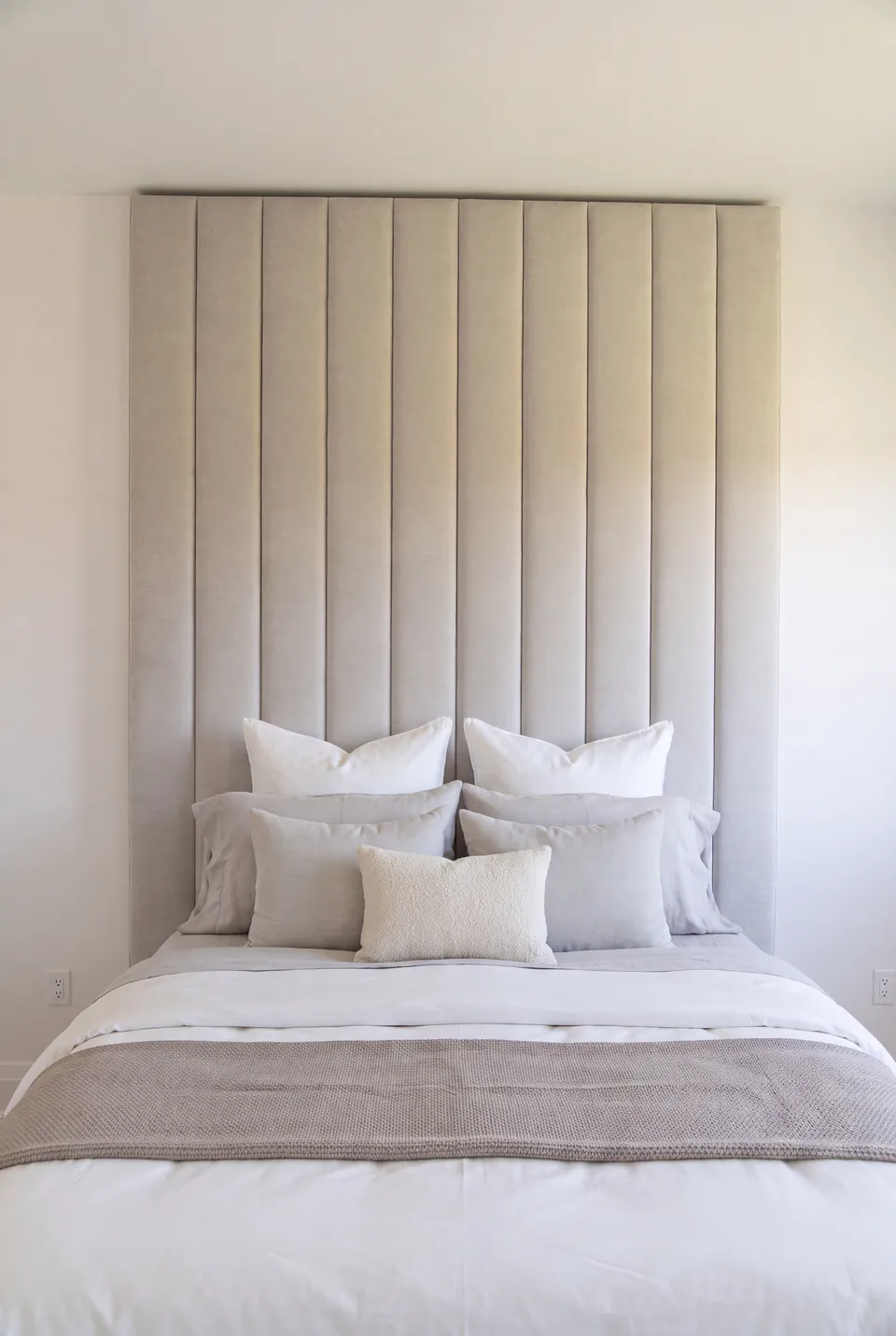 Front view of neutral bedding beneath the tall greige channel headboard.