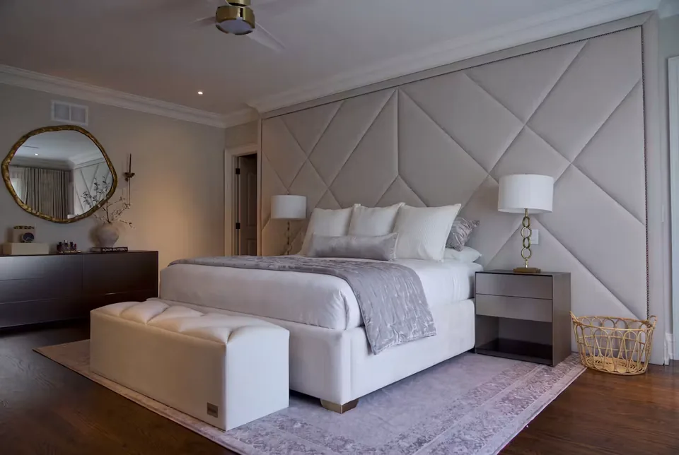 Full greige bed with a diagonal upholstered wall and pale padded bench