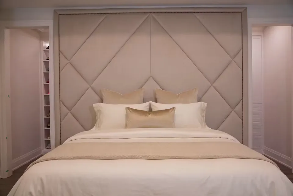Front view of a pale upholstered bed under a framed greige diamond wall