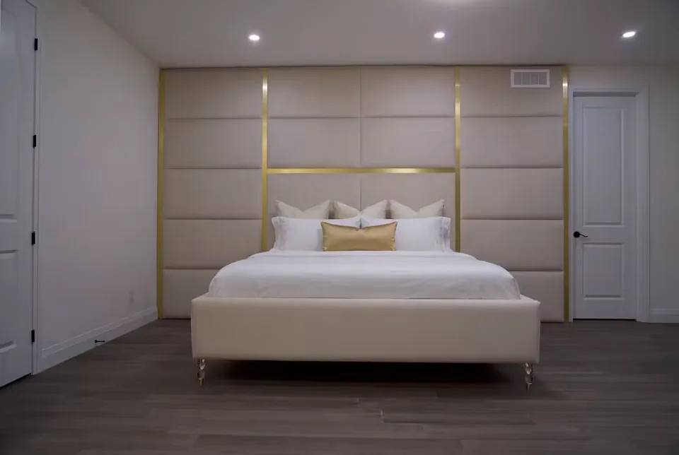 Full greige upholstered bed beneath a gold-trimmed rectangular panel grid