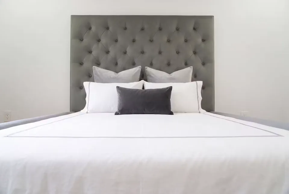 Front detail of the grey button-tufted headboard above white bedding