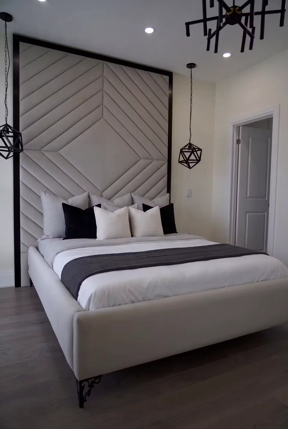 Wide view of a grey diamond-and-chevron headboard beside white shutters and black pendant lights