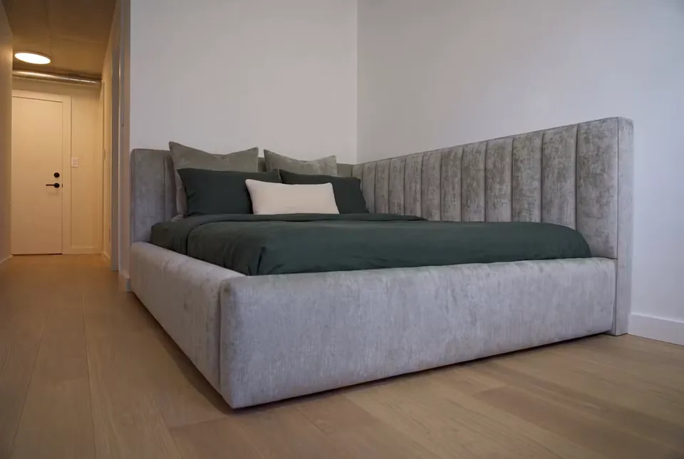 Wide view of the grey upholstered corner bed and green bedding